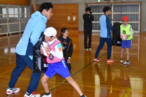 ナンバリングをつけて選手相手にタックルの練習をする児童の写真