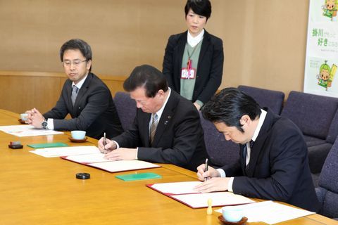 協定書にサインをする松井市長と丸山理事長の写真