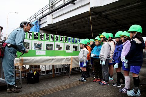 緑色のヘルメットを着けて耐震補強工事の説明を受ける児童たちの写真
