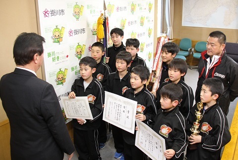 松井市長に賞状を披露する選手らの写真。トロフィーや優勝旗を持っている選手もいる。