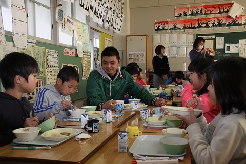 豆腐の製造業を営む橋山さんと楽しそうに給食を食べる児童たちの写真