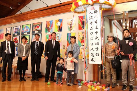中央図書館入館500万人達成記念セレモニーを受ける久道さん親子、前後賞の中山さんと松本さんと図書館関係者との記念写真の様子