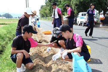 道路わきにしゃがんで小石を拾う帽子をかぶった卓球部員たち