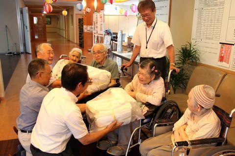 車いすの入所者に同じ目線でしゃがんで手ぬいの雑巾を手渡す協議会役員ら