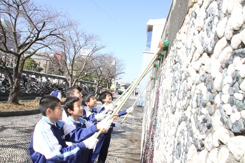 デッキブラシを使って擁壁を掃除する男子中学生