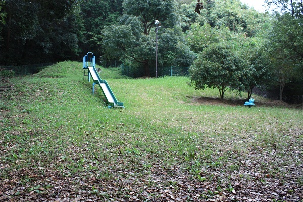 沢山の木に囲まれた自然豊かな公園、滑り台とスプリング遊具が設置されている