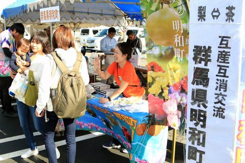 開始早々に梨やシクラメンが完売した明和町ブースでオレンジ色のTシャツを着て明るく接客するスタッフのようす