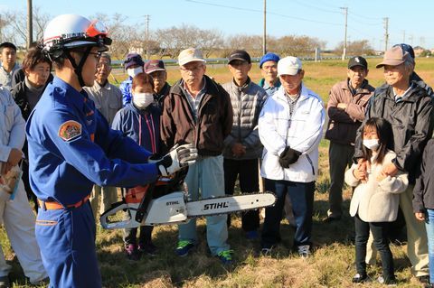 消防団員の周りに集まりチェーンソーの扱い方を学ぶ住民たち