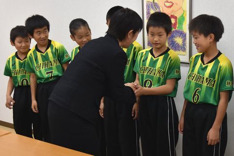 黄色と緑のユニフォームを着た千浜VSC選手6人が、山田教育長と握手をする様子