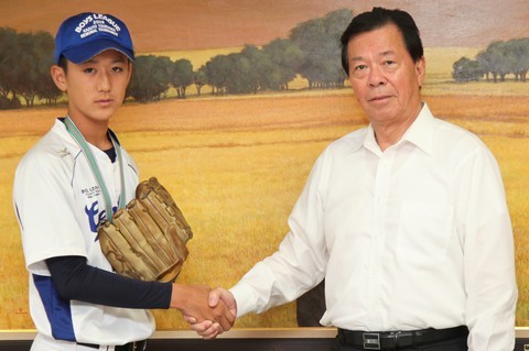 ユニフォーム姿、左手にグローブの水野さんと松井市長が握手を交わしている