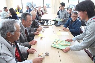 児童らがお盆にお茶やお菓子を載せ、地域の方々に配膳する様子