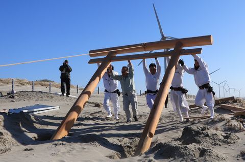 ロープで引っ張りながら、砂浜に鳥居を立てる支部員と地元の宮大工の人たち
