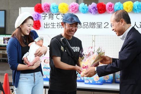 伊村副市長から出生祝い2000組達成記念の花束を受け取る河本さん夫婦と誕生したばかりの明日晴さん