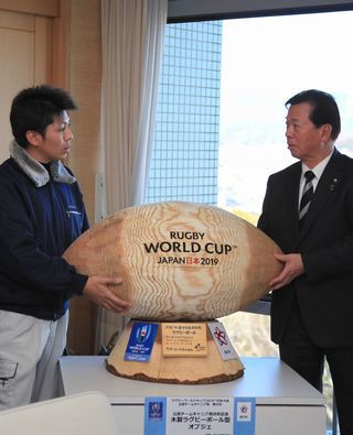 寄贈されたラグビーボールの木製オブジェの両端を持ち、向かい合う松井市長と森林組の伊達さんの写真