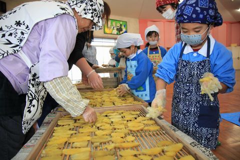 ミーナの会のメンバーの女性と干し芋づくりに挑戦する園児たちの写真