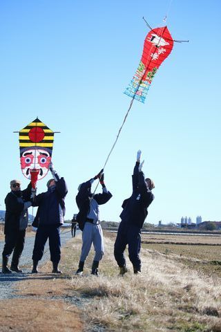 一二三会のメンバー4人が青空に遠州横須賀凧の「とんがり」など２つ凧を揚げている写真