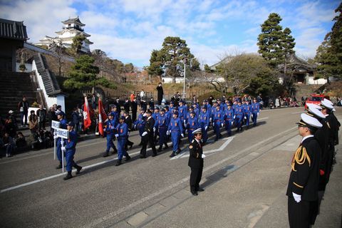 掛川城下の道路を列を作って行進する消防団員らとそれを見守る人たちの写真