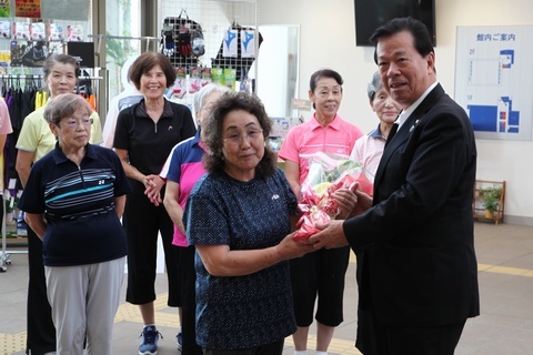 スポーツウエアを着た女性たちと、花束に手を添えている山崎さんと松井市長