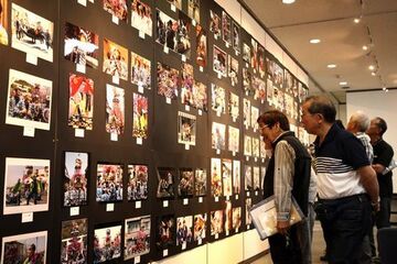 黒色の壁一面に貼られた作品をじっくりと眺める来場者たちの写真