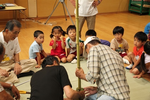 竹馬を作るボランティアらと見守る子供たちの様子。