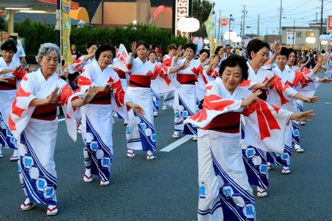 白地に赤と青の柄が入った着物の女性たちが列になって踊る様子。