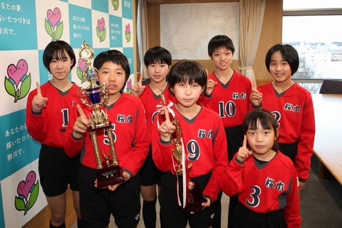 県大会優勝トロフィーを掲げ、指で1のポーズをしている桜木バレー選手たち