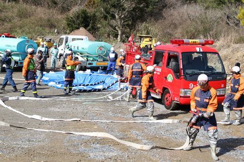 ショベルカーで掘った穴に散水車が水を補給し、消防団員が消火活動している様子