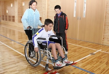 高さ3センチほどの木の障害物を協力しながら車いすで乗り越える体験する児童ら