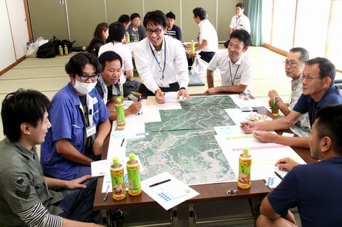 大きな地図を机の上に広げ、8人で地域の魅力を確認し合う参加者らの写真