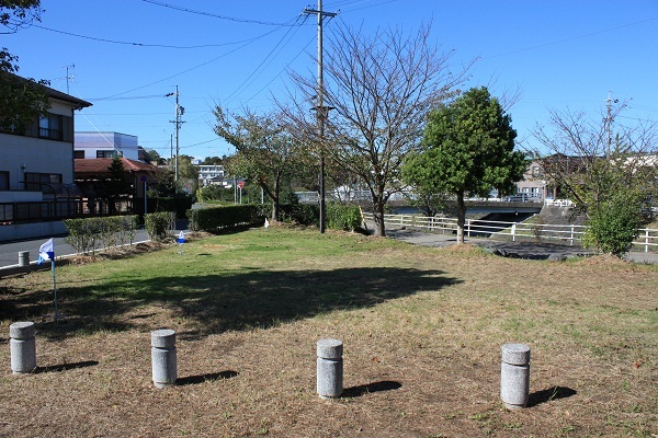 芝生と木が植わっている公園でその奥には橋と住宅が見える