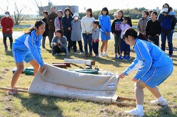 竹と毛布を使った簡易担架作りを学ぶ中学生、それを見ている住民の人たち