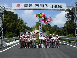 開通を祝うくす玉の下でゆるキャラと並んで記念撮影をする土方幼稚園・城東保育園の園児ら