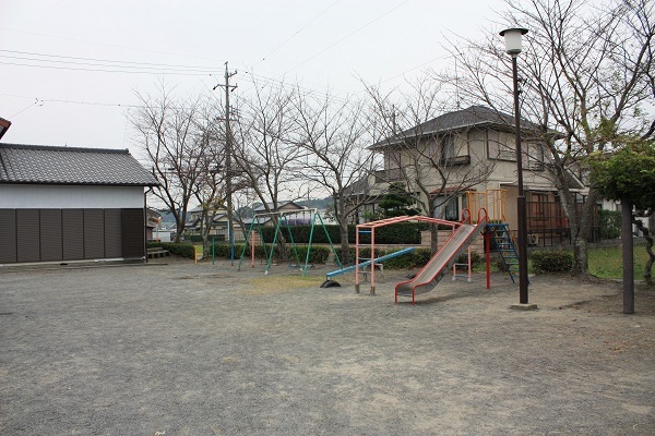 背景に住宅があり、ブランコ、シーソー、滑り台など遊具が写った公園の写真。