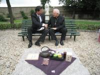 バチカンの庭園でベンチに座った松井市長と枢機卿が握手をしている様子
