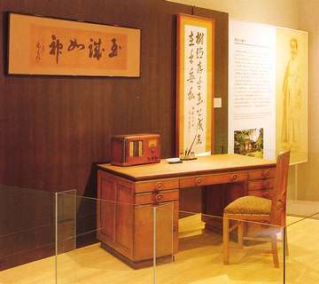 吉岡彌生愛用していた机（複製）に椅子や「至誠一貫」の書が飾られ、吉岡彌生の部屋をイメージさせるブース