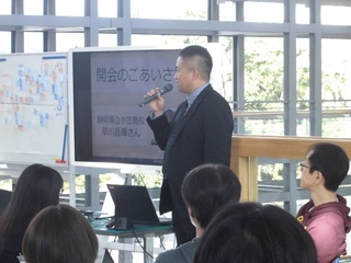 参加者の前に立ち、マイクを使って話している男性の写真