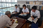 手前に市議会議員奥に子ども議員が3人机を挟んで座り質問の仕方を学んでいる