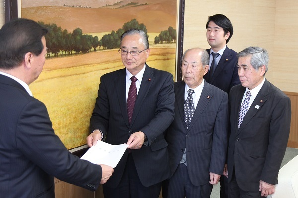 左側に松井市長提言書を挟んで右側に竹嶋善彦議長と市議会議員3名が立ち手渡している様子