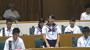 子ども議会で議員席に起立し一般質問をする女の子と周りの議員席に着席している子ども議員