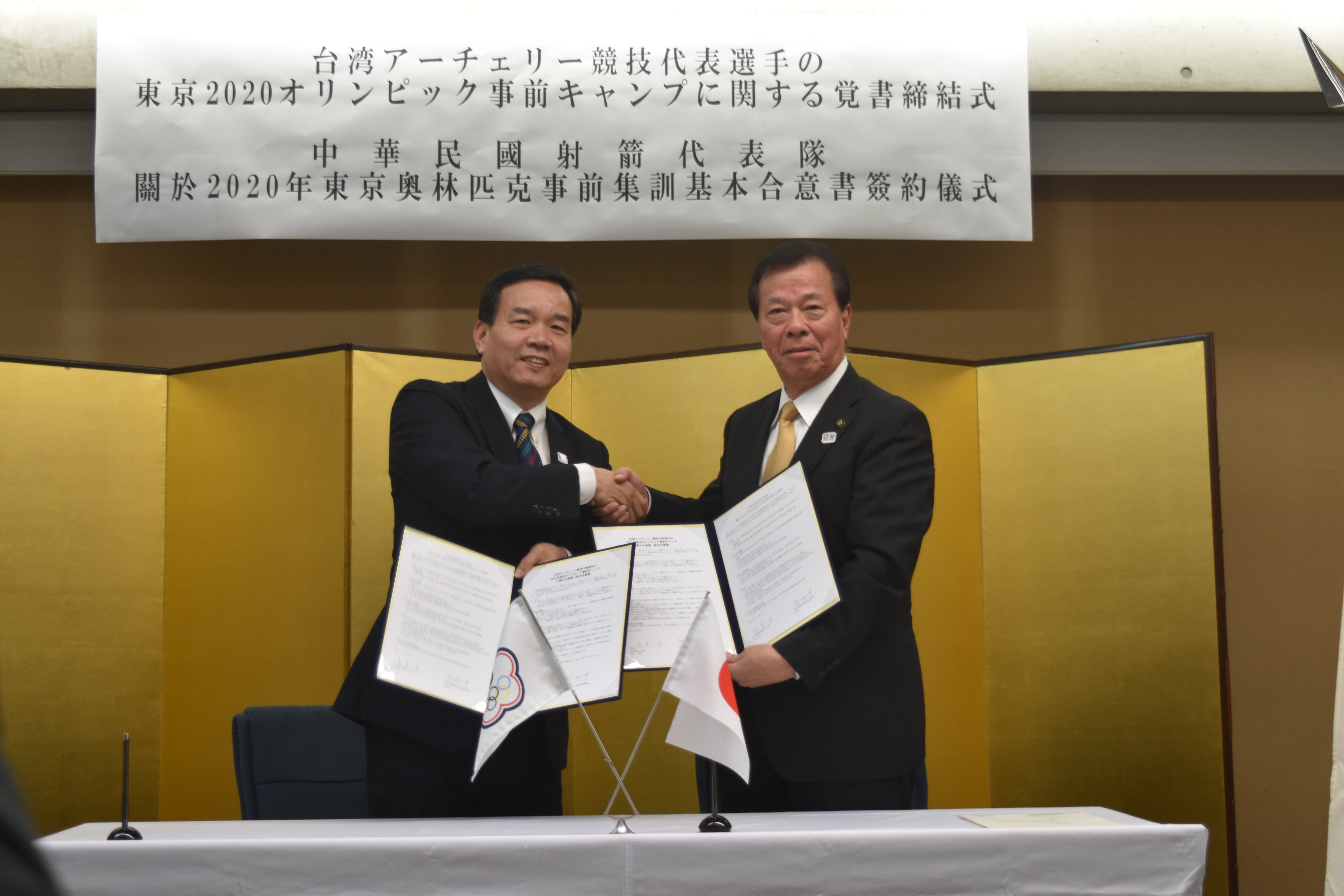 松井市長と台湾アーチェリー協会副理事長が覚書を持ち、にこやかに握手をしてカメラに視線を向けている写真