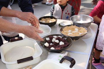 餅にきなこやアンコをまぶしている大人と、近くで見ているこども達。