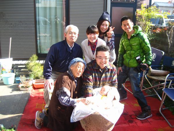 玄関先にて記念撮影。臼に入れた初孫を囲み、笑顔の家族たち。