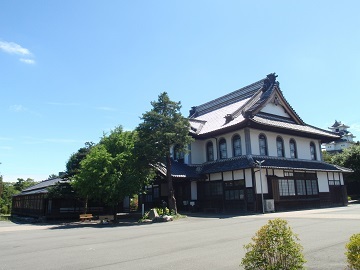 大講堂の建物外観。日本瓦の大屋根、漆喰塗りの外壁、洋風の丸みのある窓が特徴的である。
